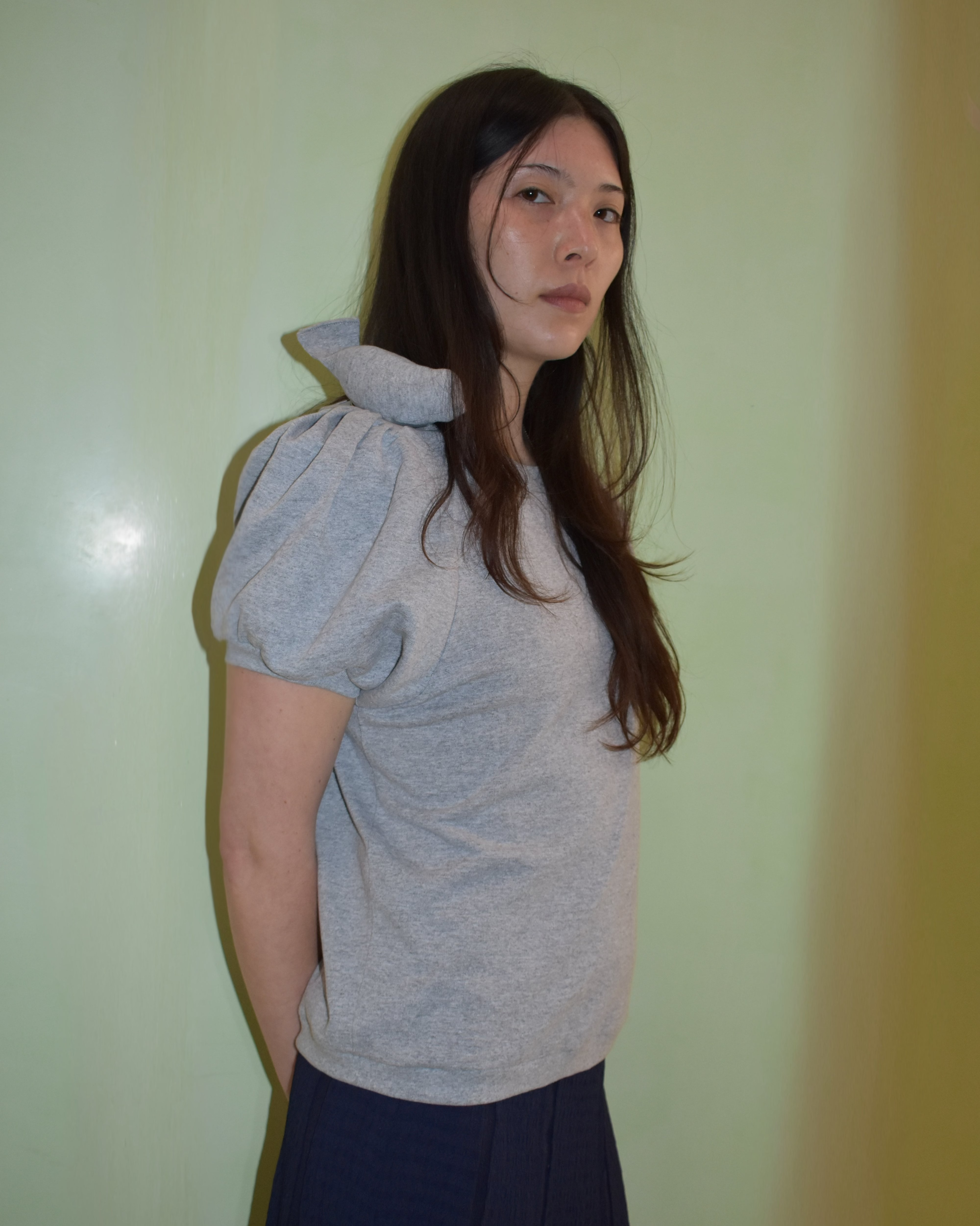 Person wearing a gray top with puffed sleeves against a light green wall.