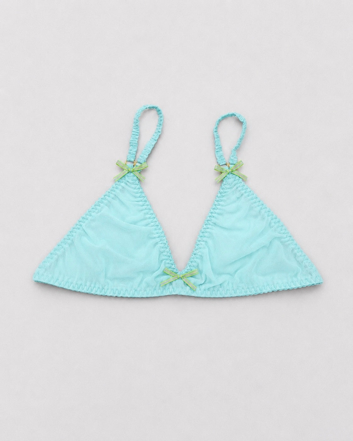 Flat-lay product photo of a delicate triangle bralette in sheer aqua mesh with ruched cups, matching ruched straps, and small lime green ribbon bows at each strap and the center front, photographed on a light gray seamless background with soft, even studio lighting.