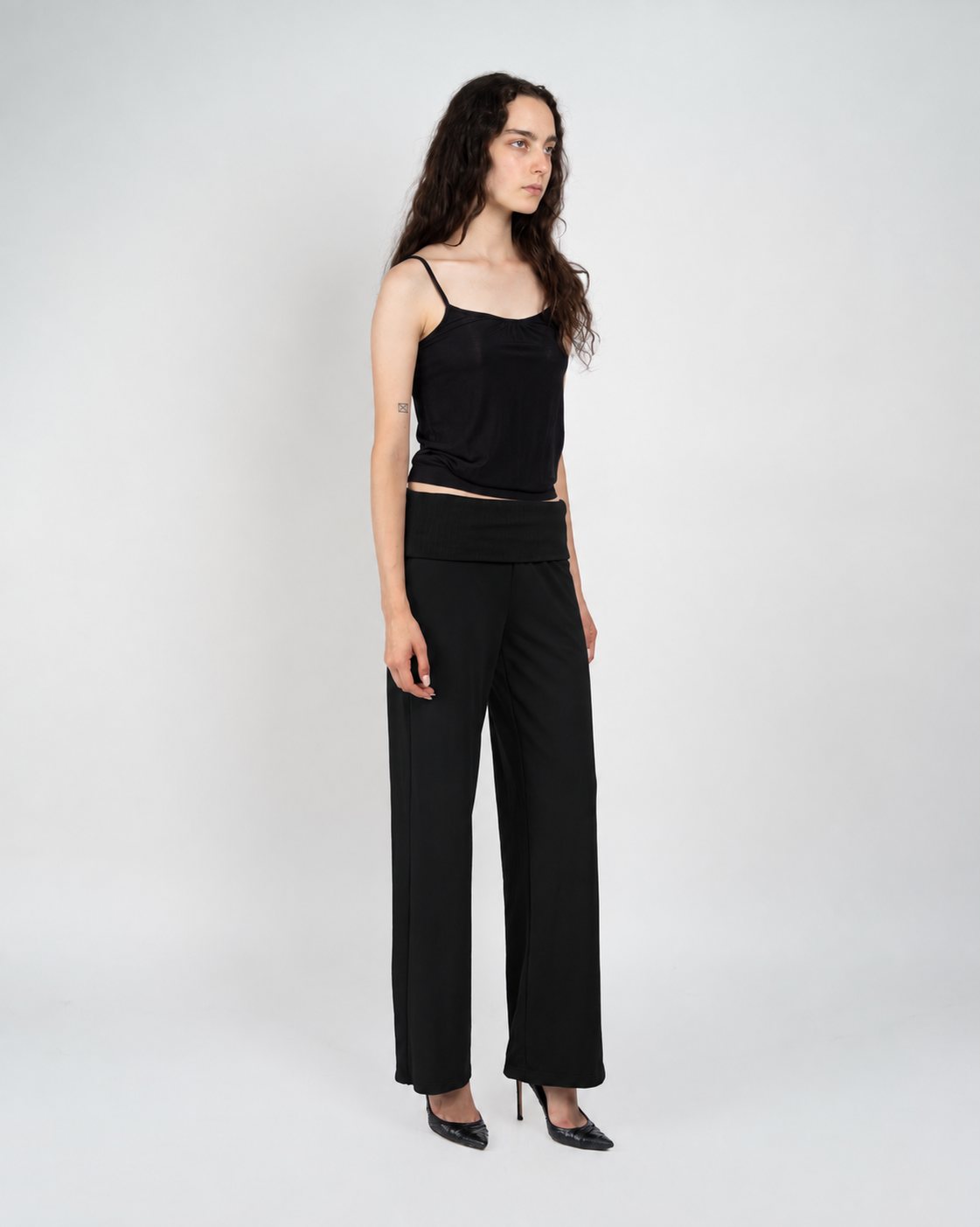 A woman modeling a black camisole top and black wide-leg trousers against a light gray studio background.