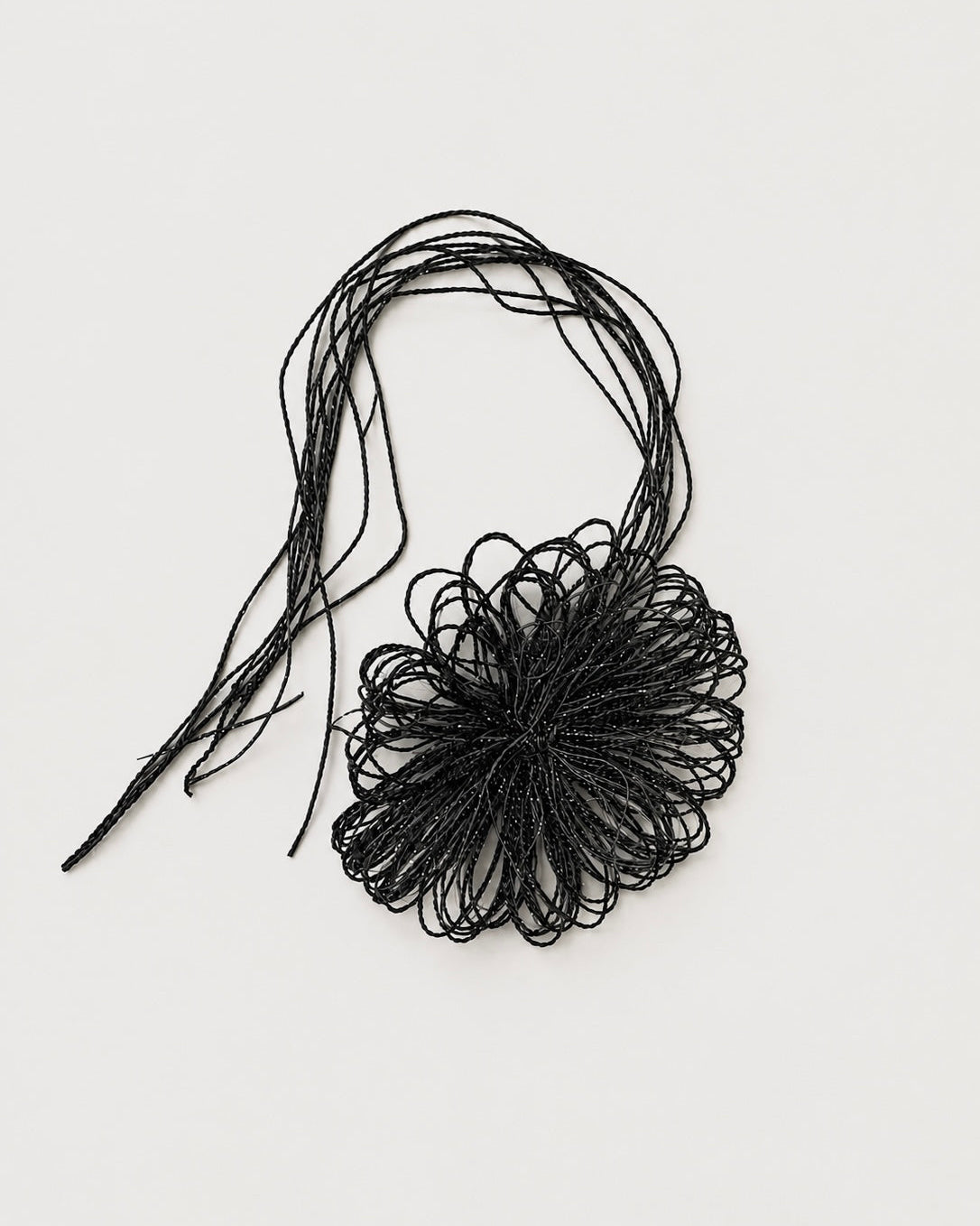 A black beaded fringe necklace with a large, textured flower-like bead cluster and long thin strands, displayed on a clean off-white background.