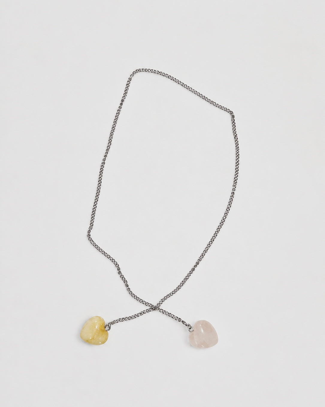 A delicate silver chain necklace featuring two small, heart-shaped stone pendants, one pale yellow and one light pink, displayed on a clean light gray background.