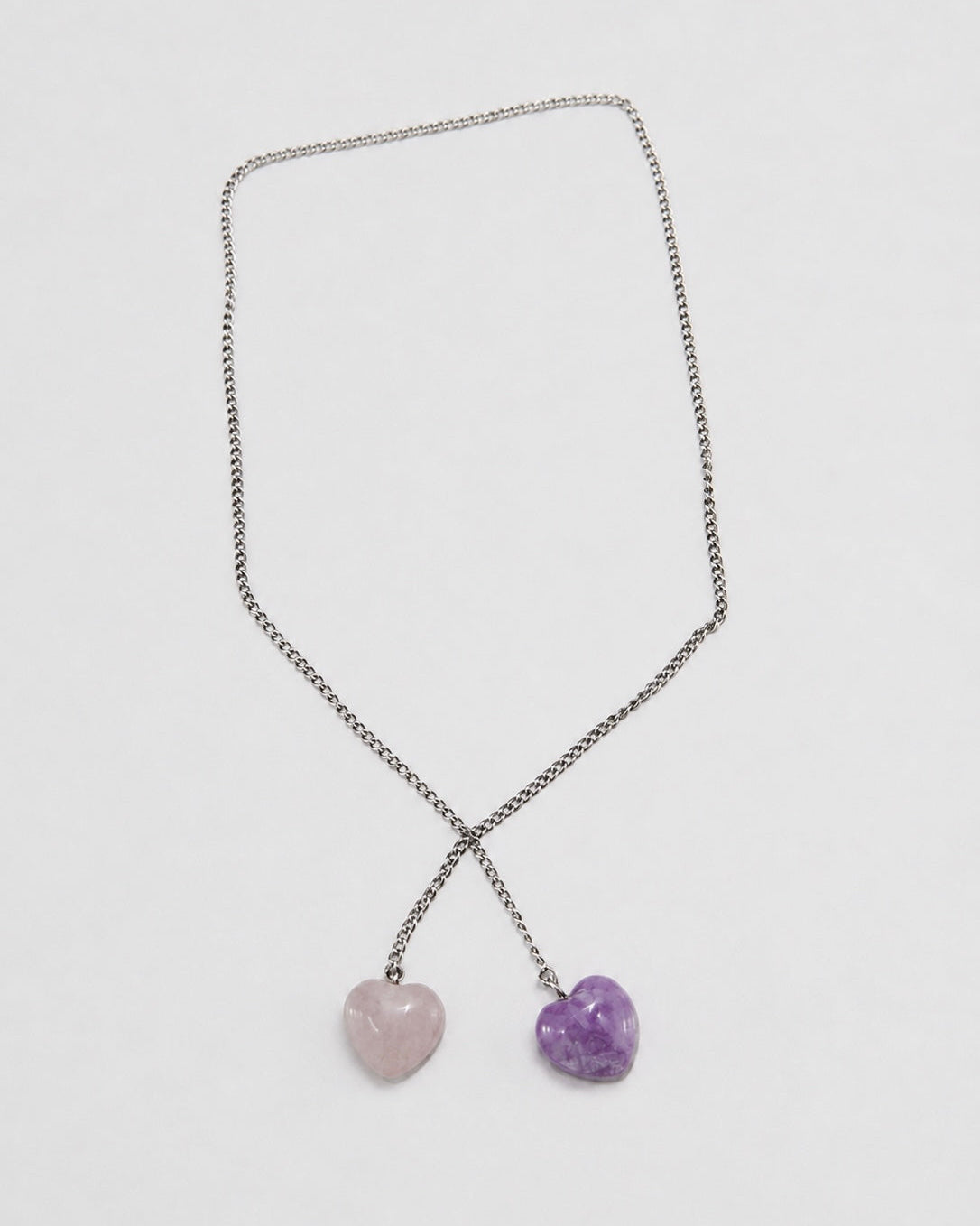 A silver-toned chain necklace with two dangling heart-shaped pendants, one light pink and one purple, displayed on a clean white background.