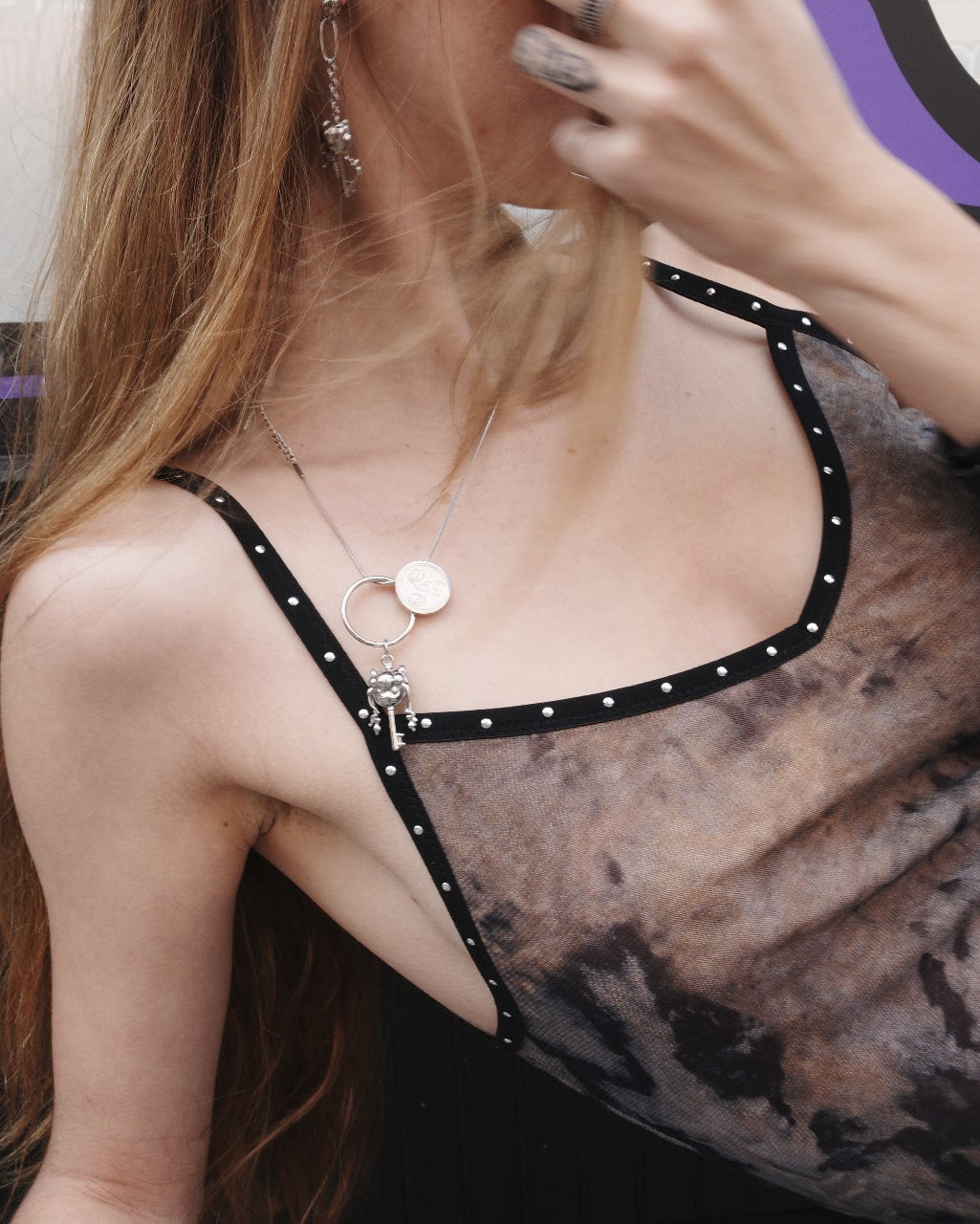 Person wearing a sheer top with black straps in a dimly lit room.