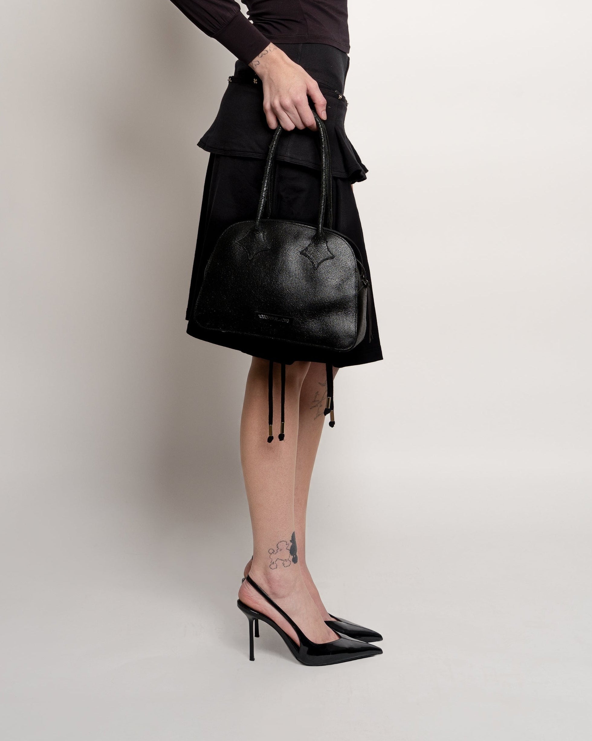 Person wearing a black skirt and holding a black handbag on a plain background