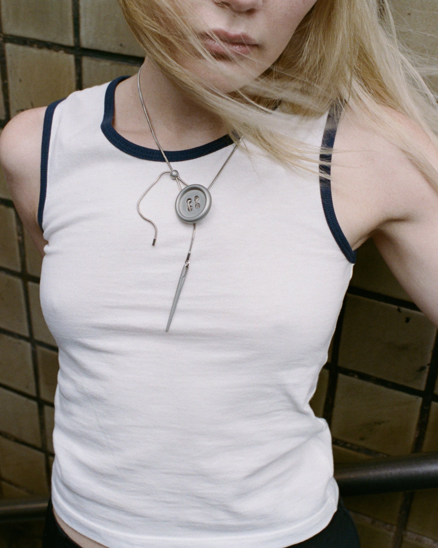 Person wearing a white tank top with black trim in a tiled room