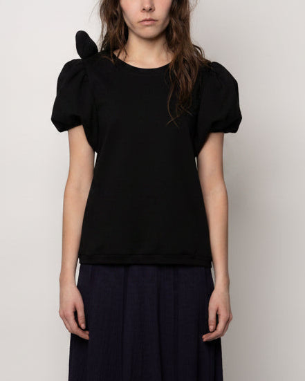 Person wearing a black top with puffed sleeves against a plain background