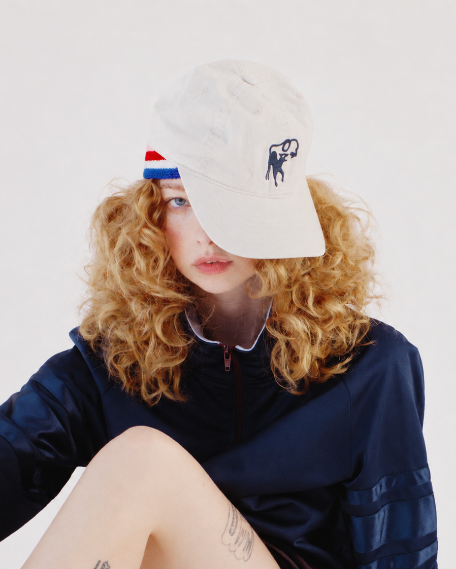 Person wearing a white cap with a logo, sitting against a plain background