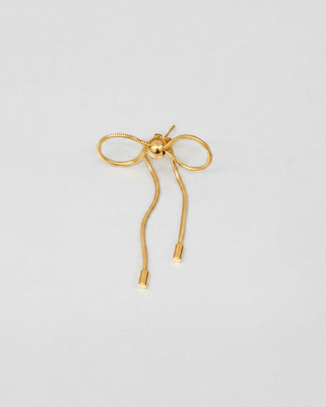 A delicate gold bow-shaped earring with a small central bead and straight dangling ends, photographed on a plain light gray background.