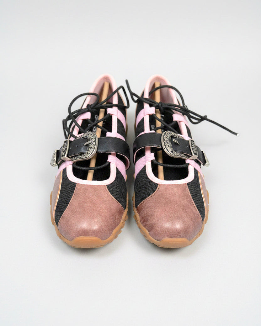 Pair of pink and black low-profile sneakers with lace-up detail and decorative buckle straps, shown on a clean light gray studio background.